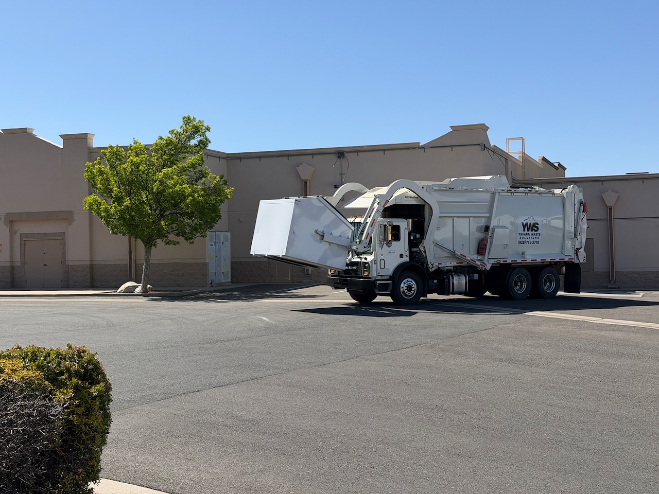 YWS front-load truck servicing a dumpster at a local business